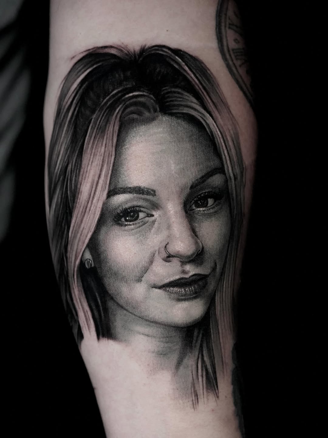 Monochrome portrait of a woman with shoulder-length hair and small earring, rendered in photorealistic grayscale on arm.