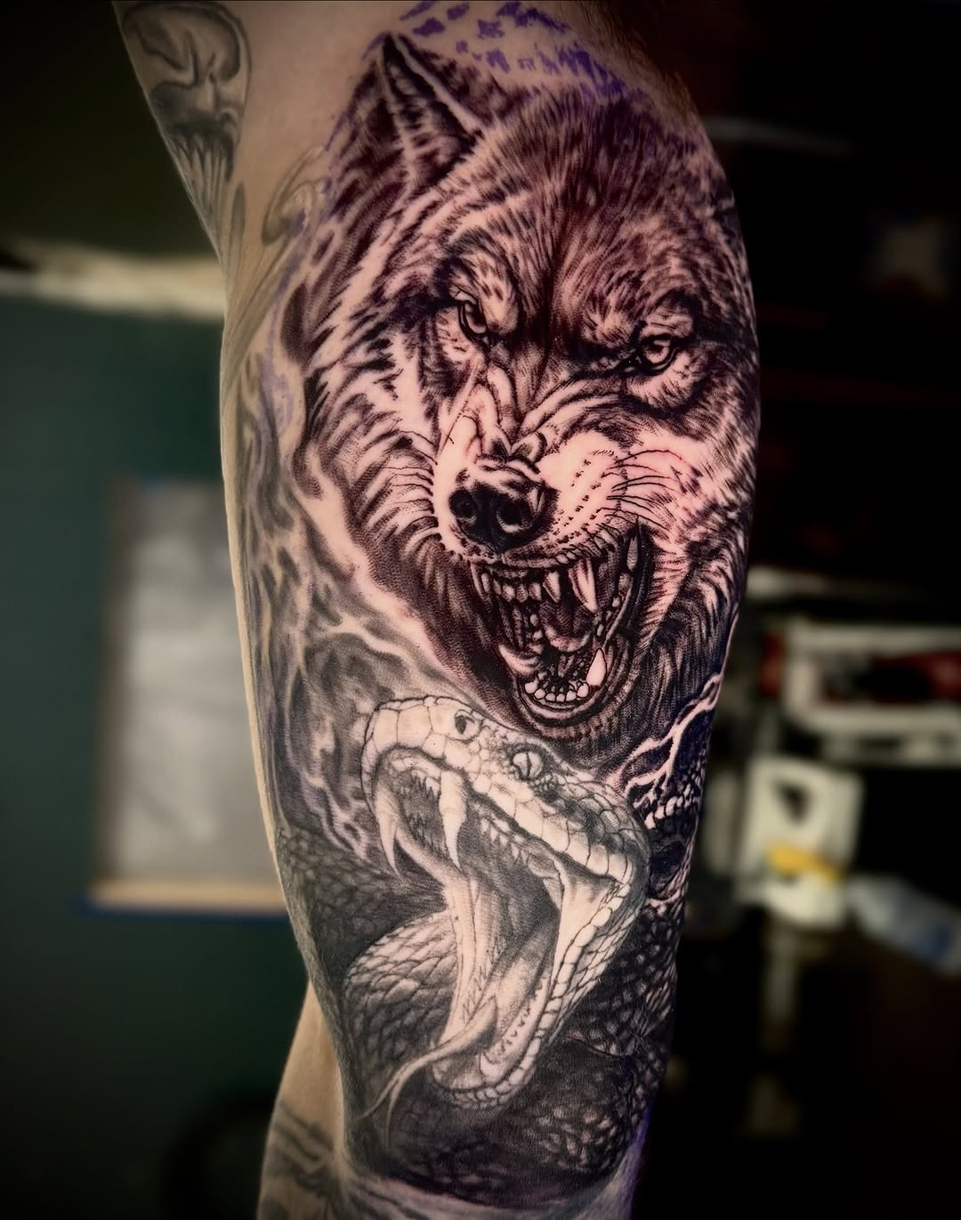 Black and grey tattoo of a snarling wolf head above an open-mouthed snake, shaded arm sleeve piece.