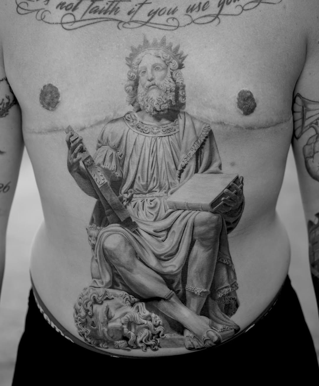 Detailed monochrome portrait of a bearded robed figure with crown holding a sword and tablet, centered on chest.