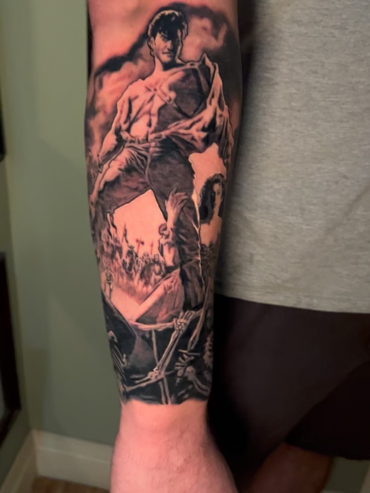 Black and grey realistic portrait tattoo of a man in dramatic pose on forearm with skeletal imagery below.