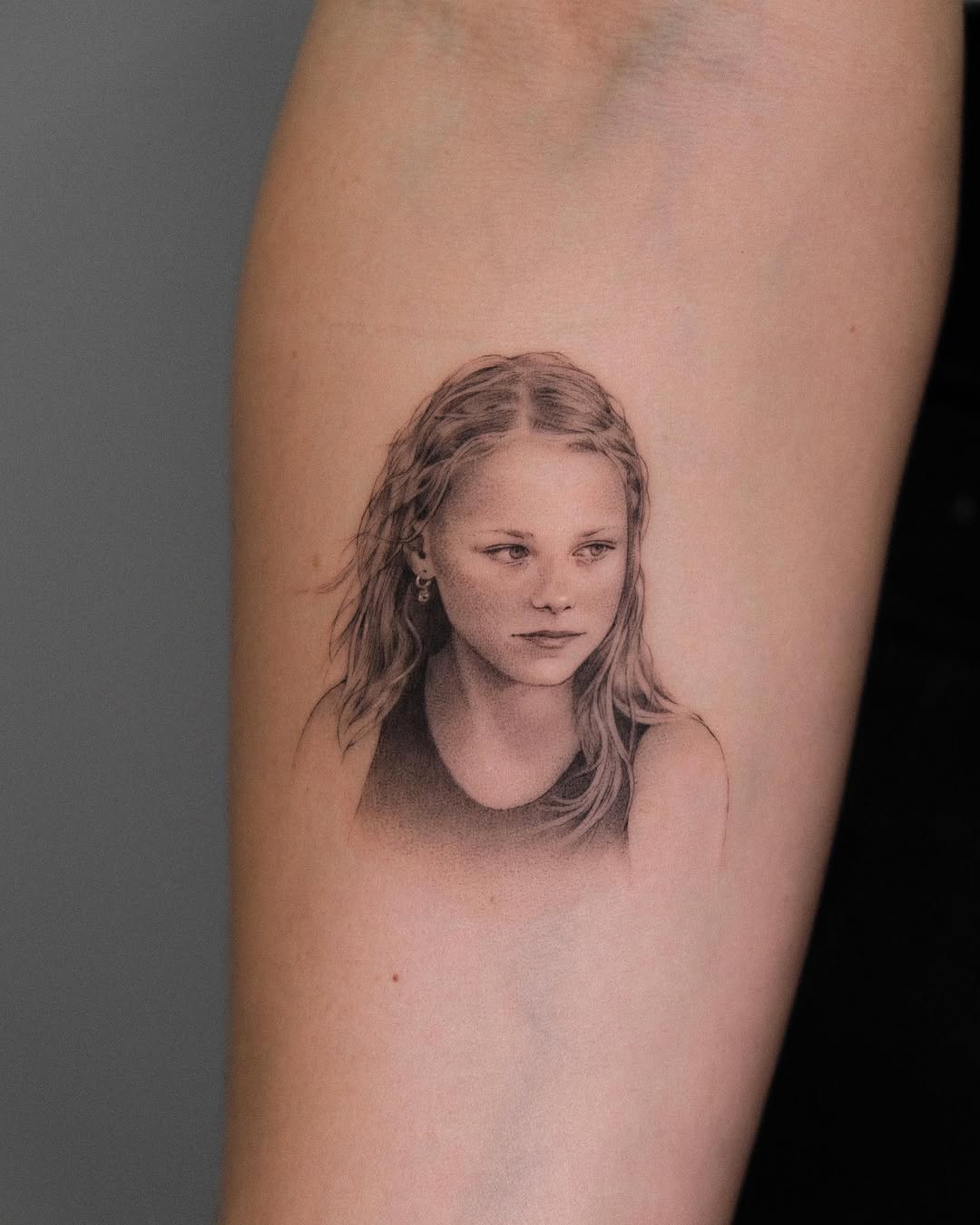 Monochromatic portrait of a young girl with long wavy hair, looking downward, on upper arm.