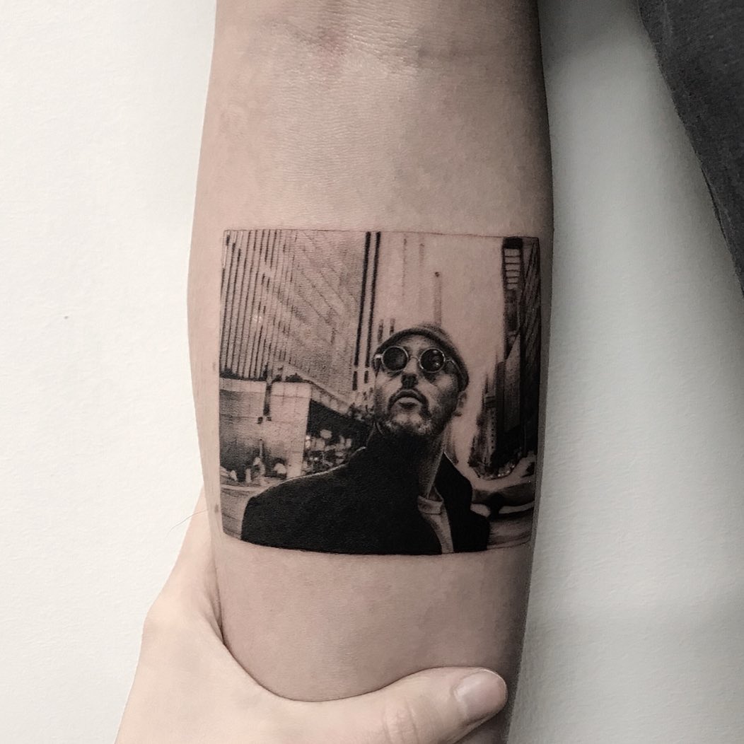 Black and grey photorealistic portrait of a man wearing round sunglasses on the inner bicep.