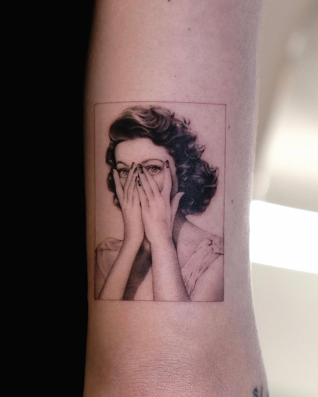 Monochromatic portrait of a woman with vintage-styled wavy hair, hands covering lower face, on inner arm.