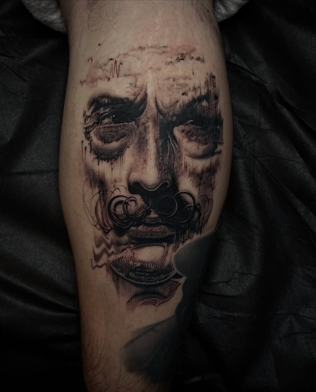 Black and grey portrait tattoo of a bearded man's face with closed eyes on the calf, featuring detailed shading and stippled effects.