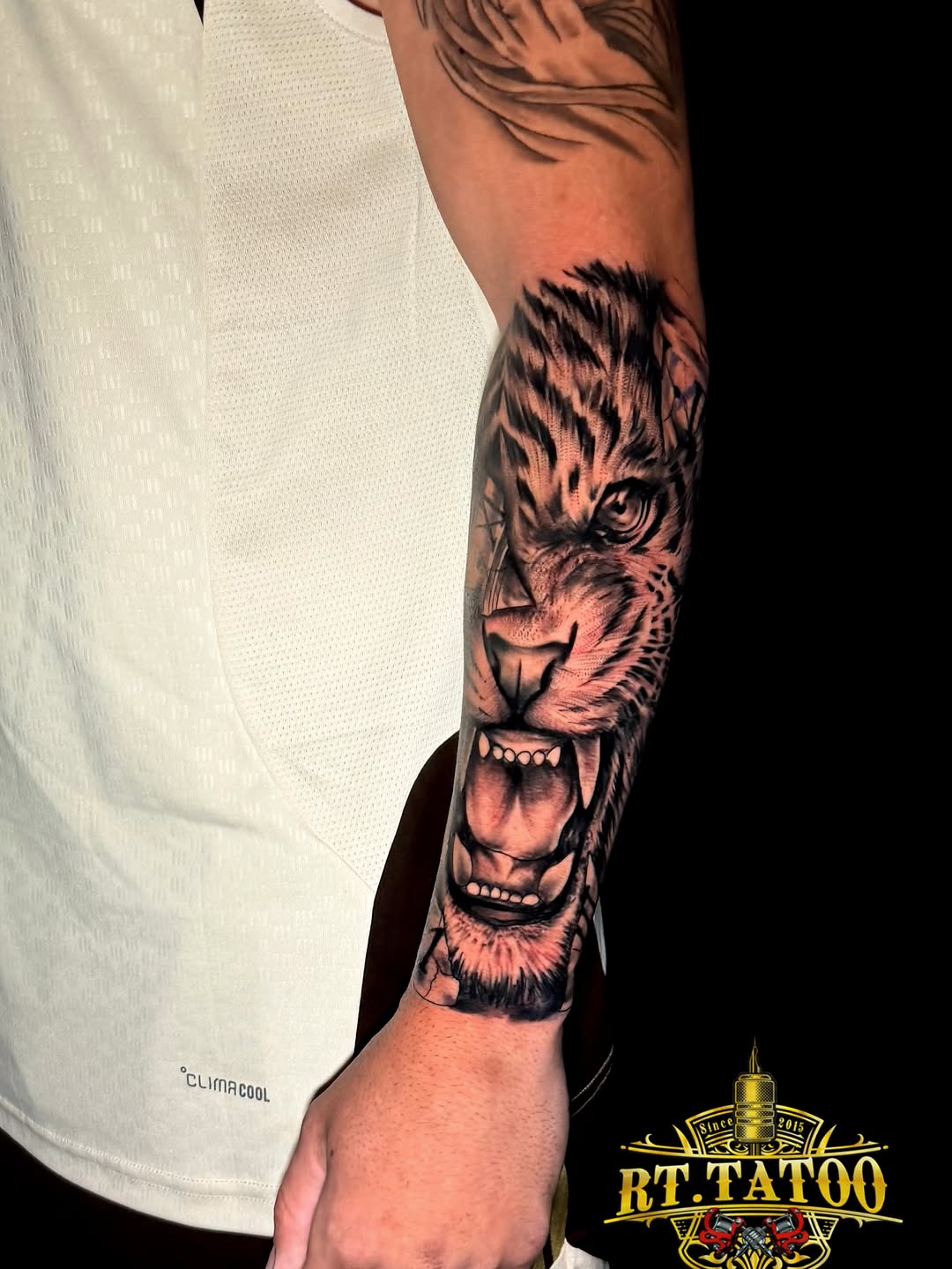 Realistic tiger head with open mouth showing teeth, rendered in black and grey on forearm.