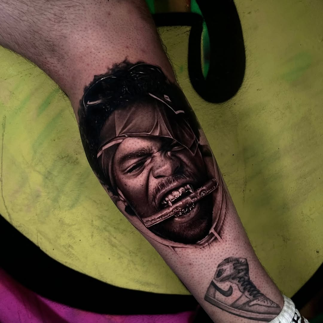 Black and grey portrait tattoo of a man's face with sunglasses and cigar on forearm, with sneaker tattoo below.