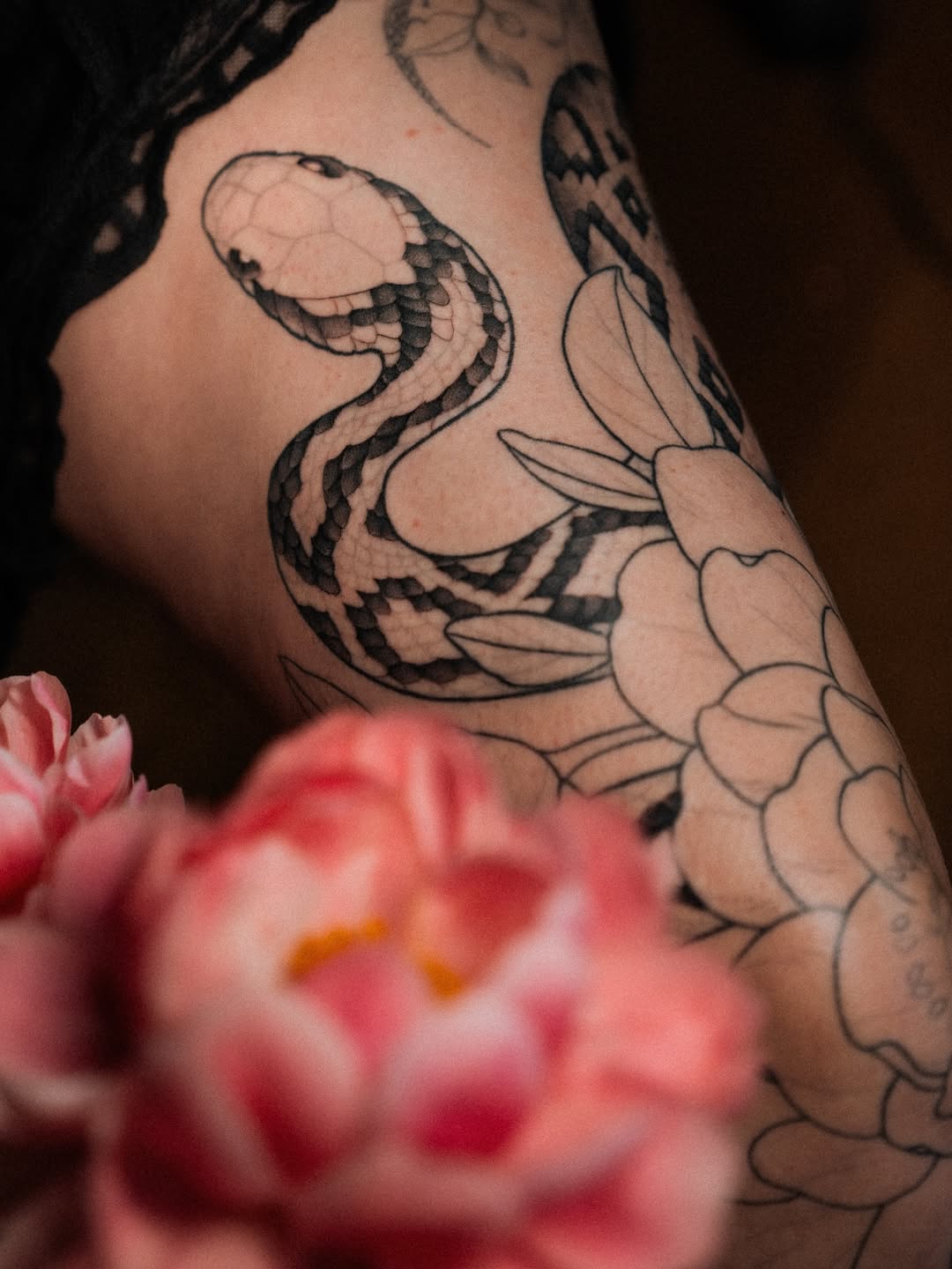 Black and grey snake and floral tattoo on upper arm with scaled detailing and botanical elements.