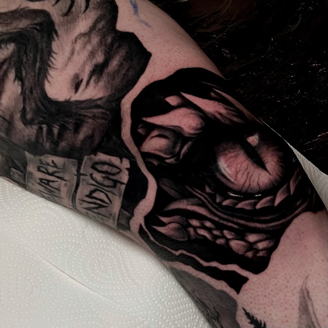 Photorealistic black and grey portrait of a hooded skull face with detailed shading on the upper arm.
