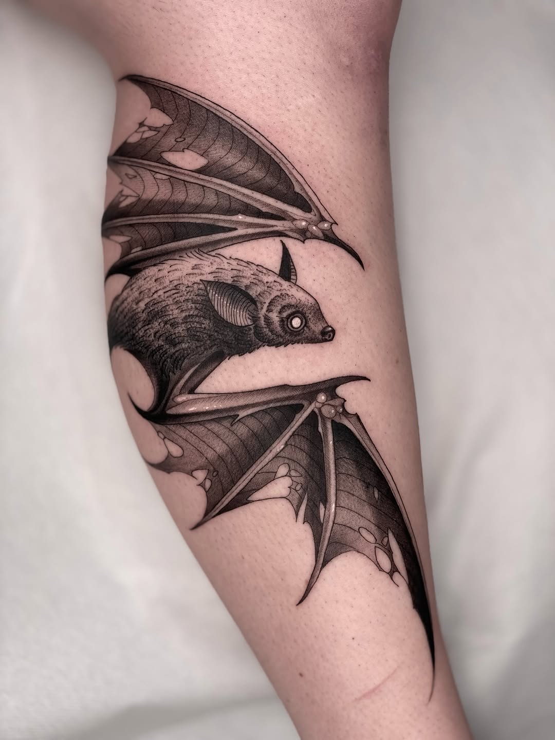 Two detailed bats with extended wings in black and grey ink on the upper arm, rendered with fine shading and anatomical precision.