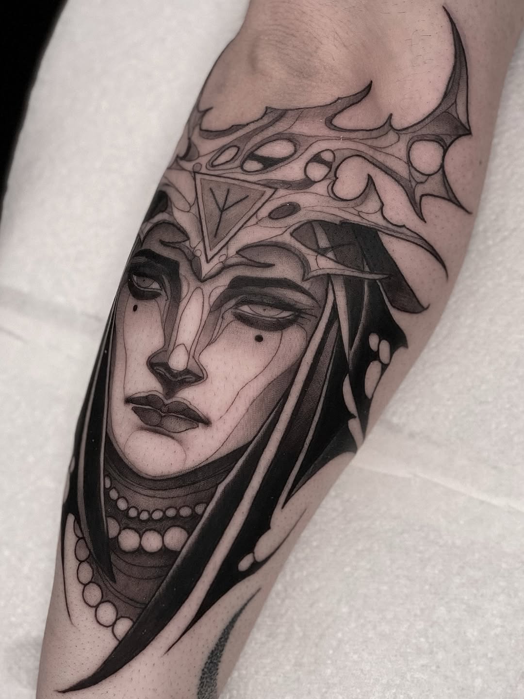 Black and grey portrait of a mystical woman with ornate headdress and beaded necklace on leg, realistic shading.