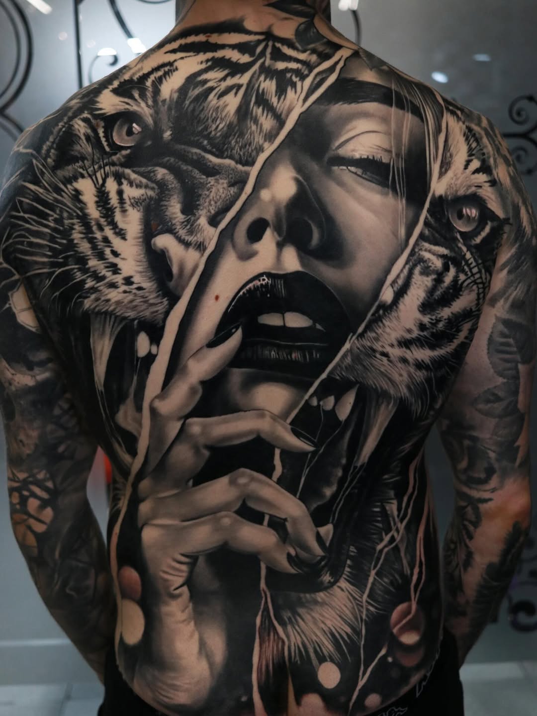 Black and grey back tattoo featuring a woman's face with tigers flanking both sides, detailed realism with smooth shading.