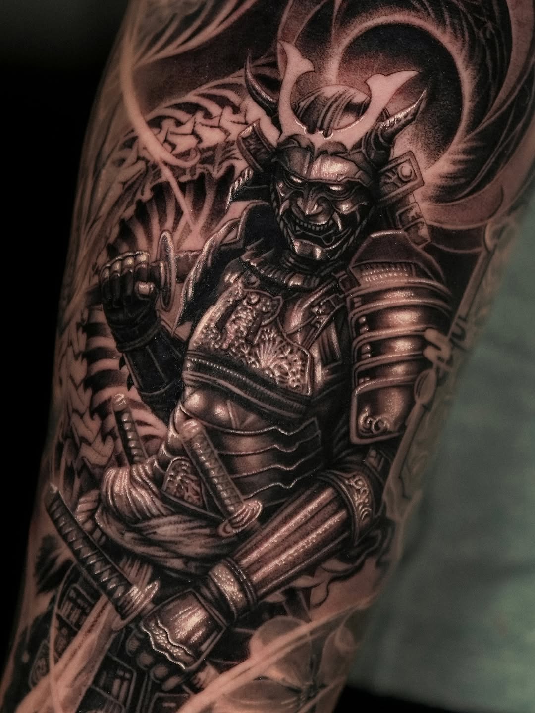 Black and grey demon warrior in ornate samurai armor with horns and menacing expression on upper arm.