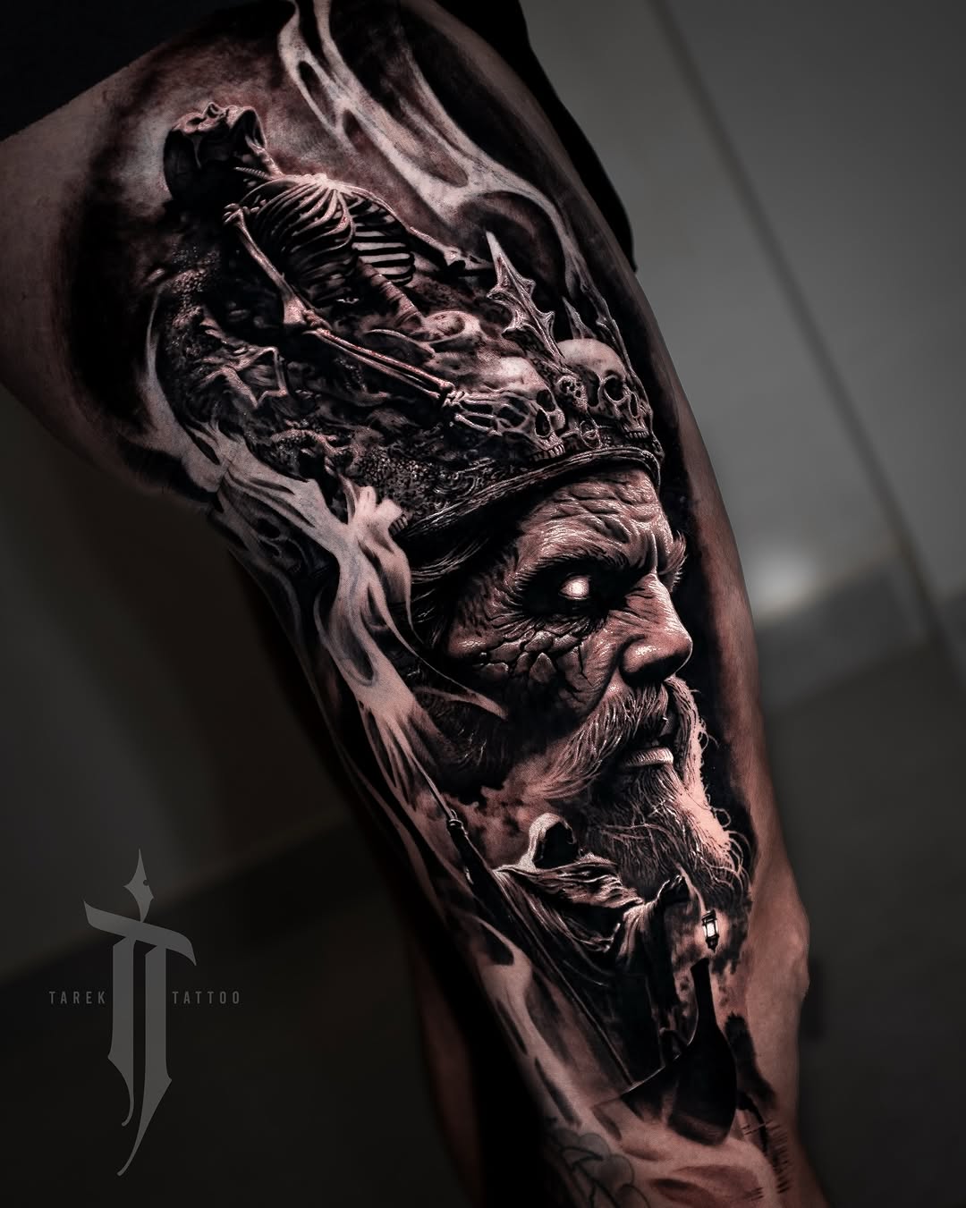 Black and grey portrait tattoo of a bearded man with skeletal imagery and a rat above on upper arm.