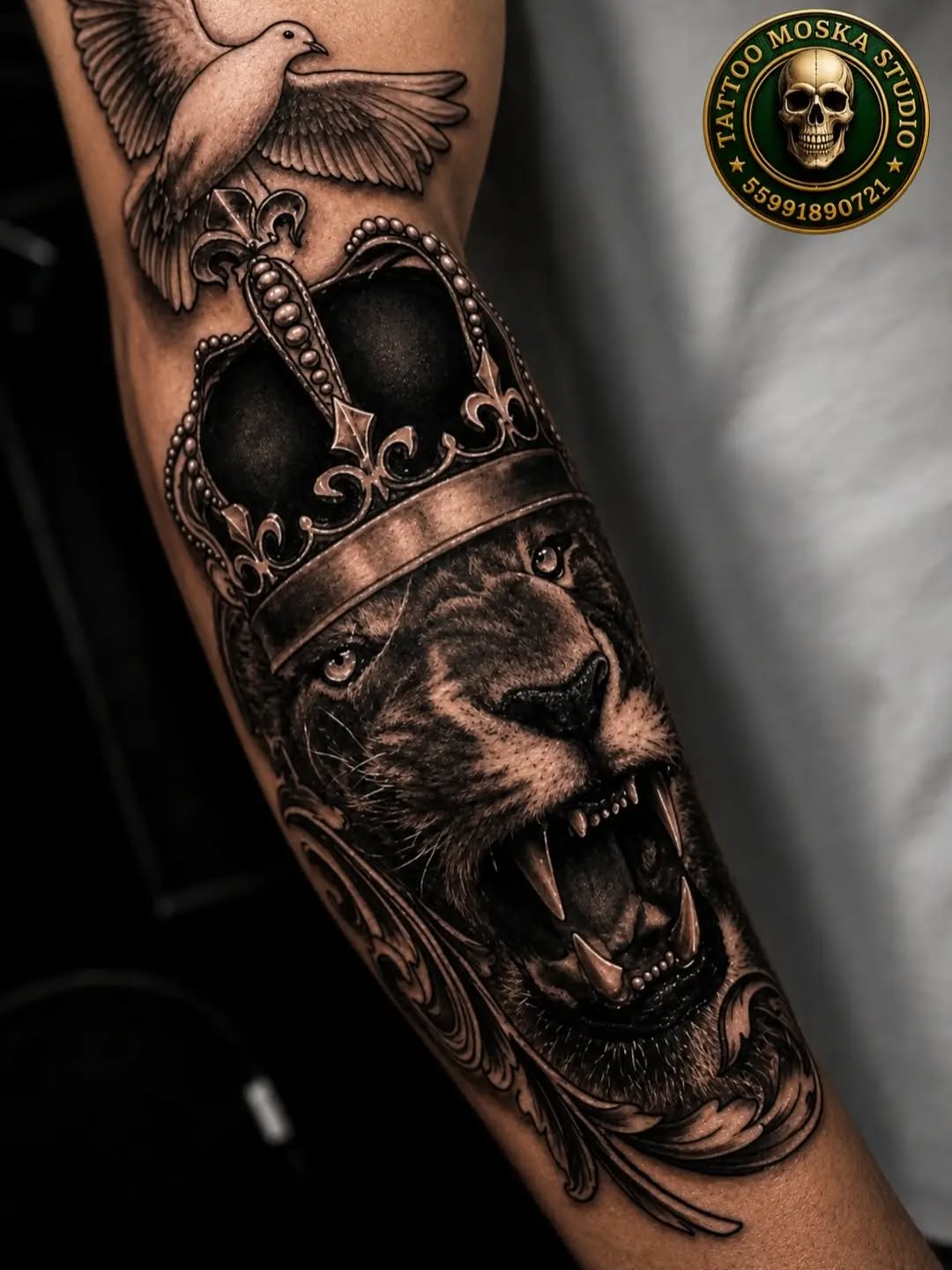 Lion wearing ornate crown with dove perched above, rendered in black and grey on forearm with decorative scrollwork.