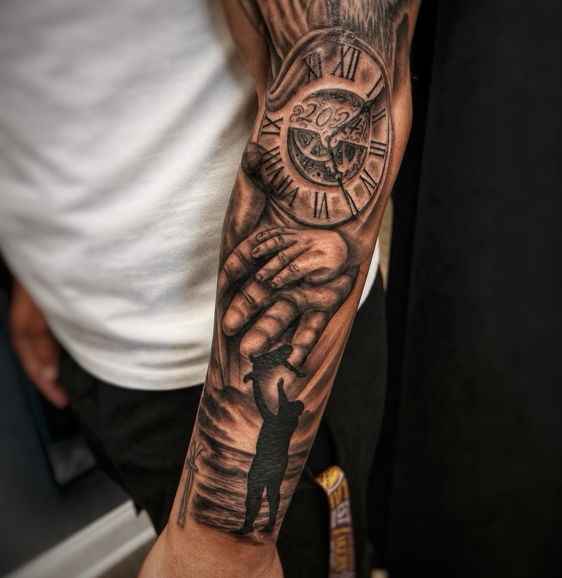 Black and grey full sleeve tattoo featuring a detailed Roman numeral clock with gears, holding hands, and a silhouetted figure on the forearm.