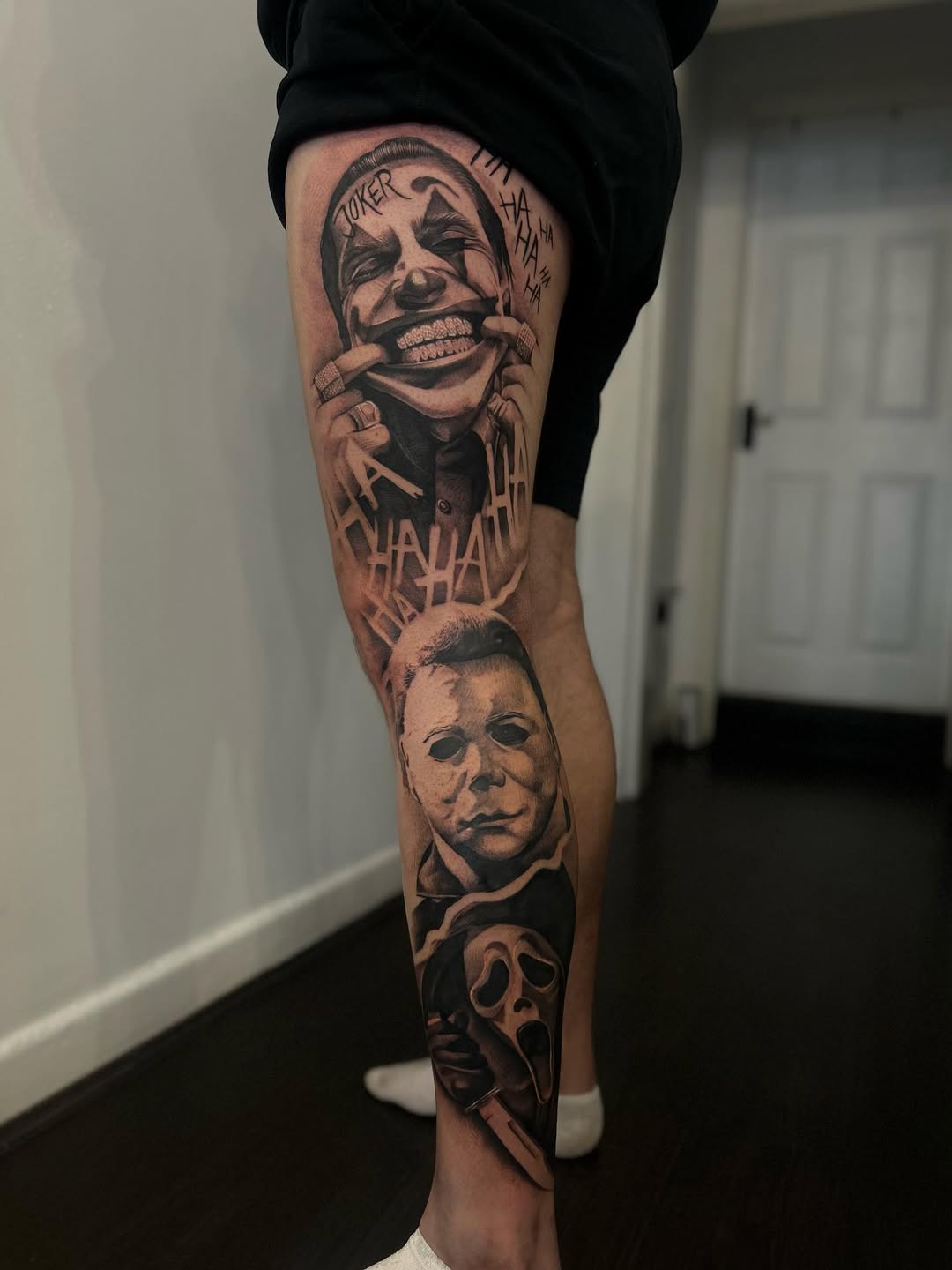 Black and grey leg sleeve featuring horror movie characters including a laughing clown face, masked killer, and screaming ghost face on the thigh and calf.
