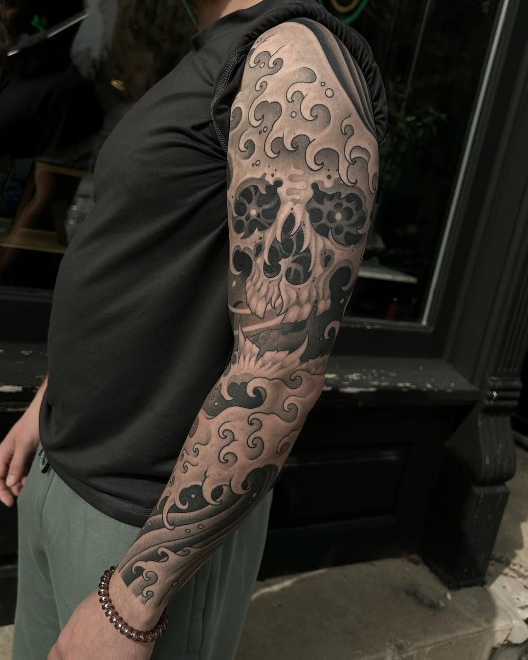 Large decorative skull tattoo with ornamental swirls covering the entire arm from shoulder to wrist in black and grey.