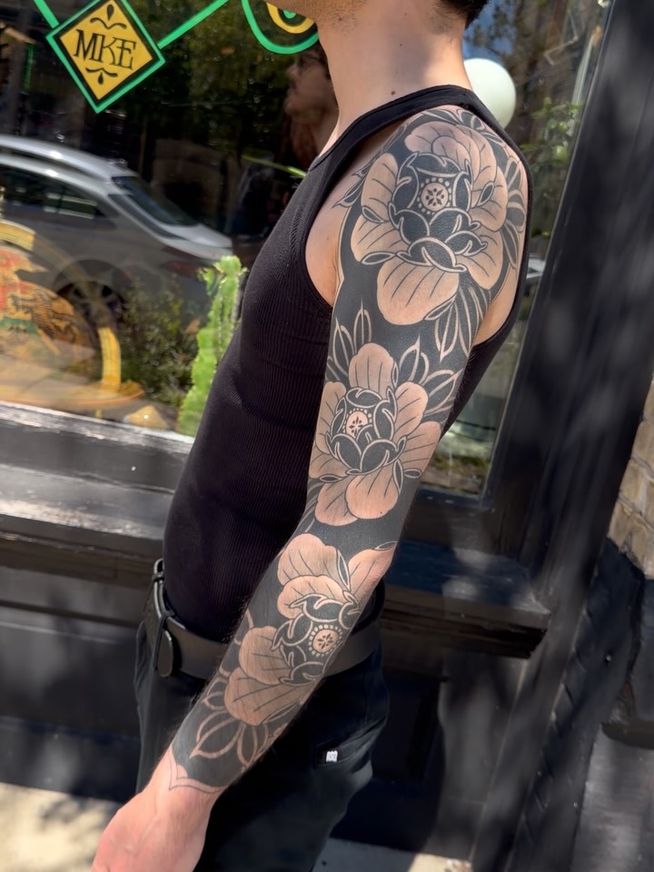 Full black and grey floral sleeve tattoo featuring large peonies with detailed linework and soft shading on arm.