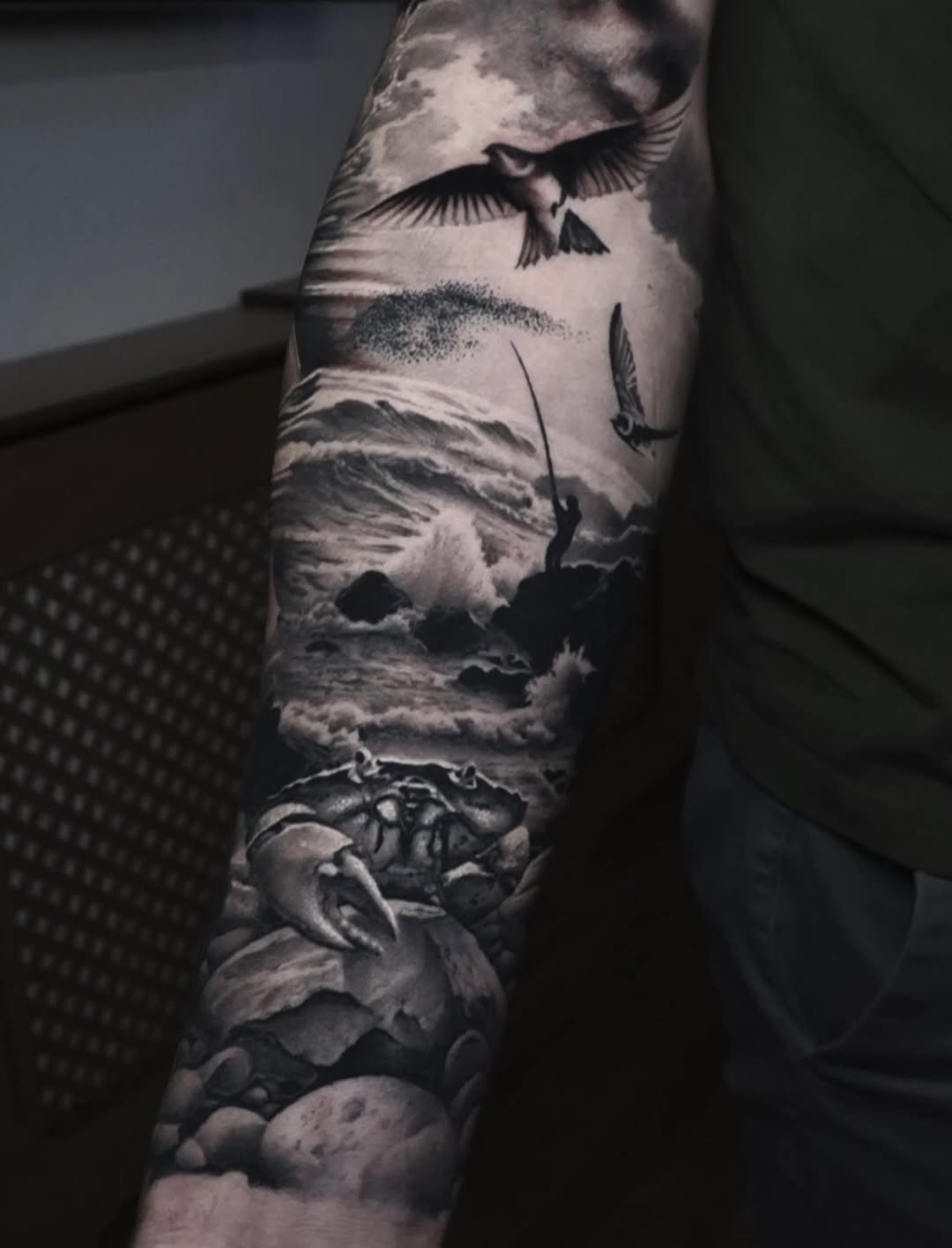 Monochromatic sleeve tattoo featuring birds in flight, stormy clouds, and floral elements on the forearm.