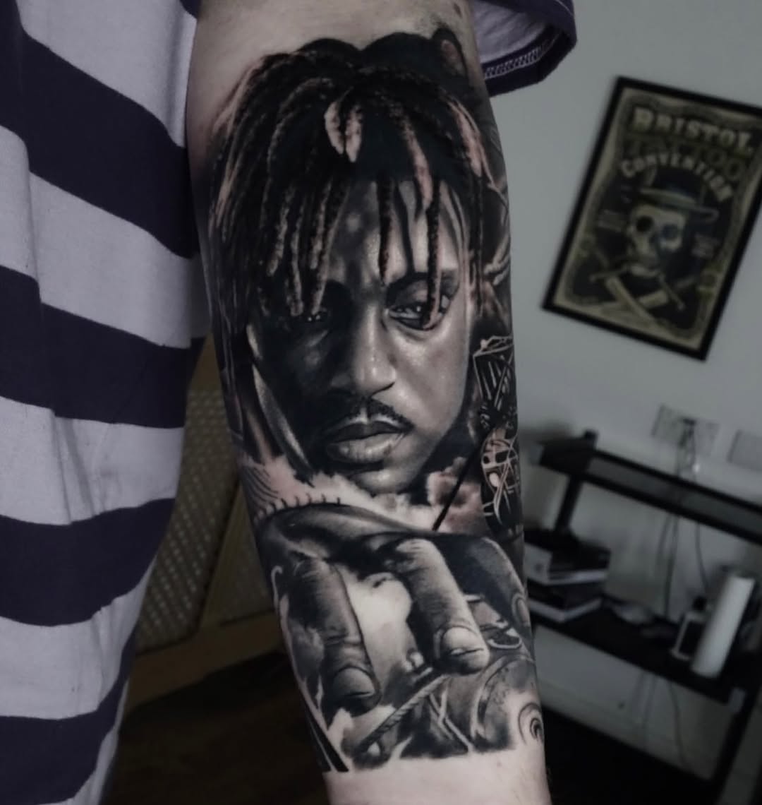 Monochrome photorealistic portrait tattoo on upper arm featuring a person with dreadlocks and contemplative expression.