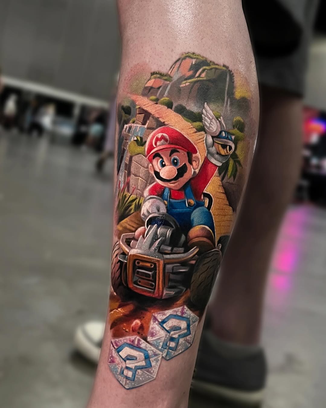 Mario in a red cap riding a mine cart with Bullet Bill and castle scenery, rendered realistically in full color on a lower leg.