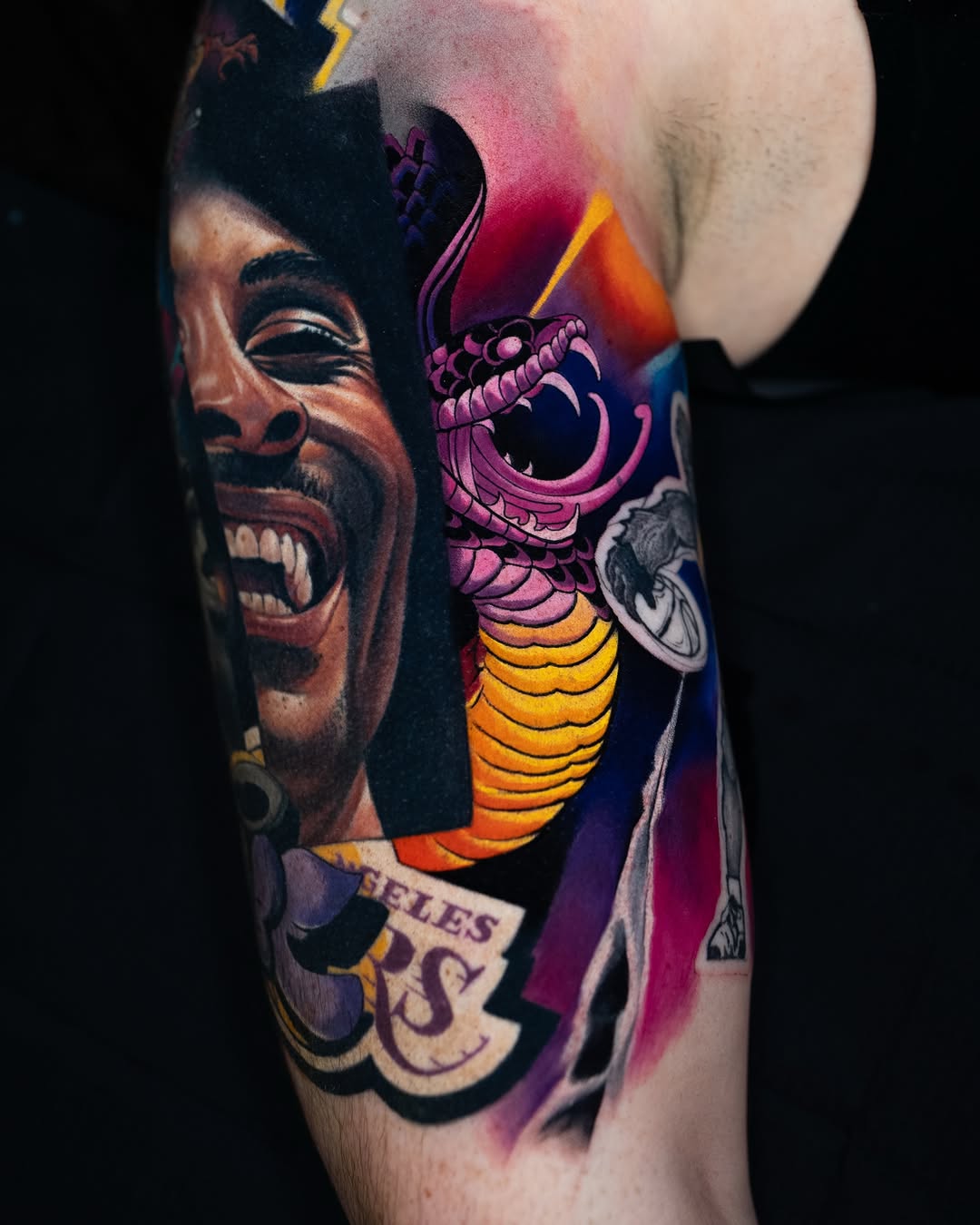 Colorful sleeve tattoo featuring a smiling man's portrait, a purple demon creature with fangs and yellow segmented body, and lettering on upper arm.