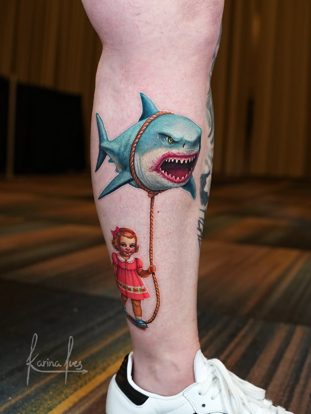 A child in red dress holding a rope leash connected to a large aggressive shark with open mouth on the calf.