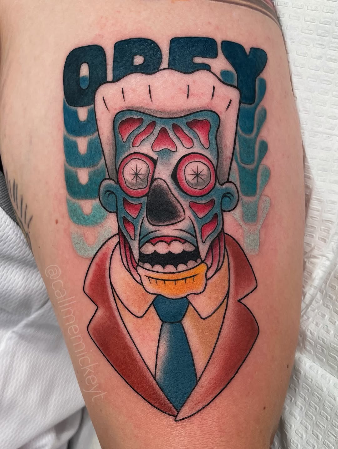 Finished skull tattoo with red eyes and orange mouth wearing a red jacket and blue tie on upper leg.