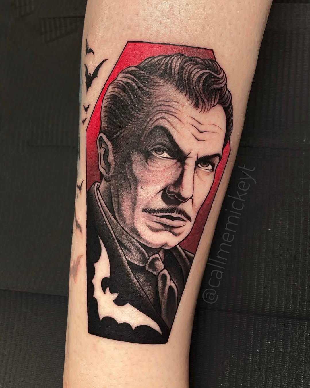 Portrait tattoo of a man's face with styled hair on upper arm, featuring red background and black shading.