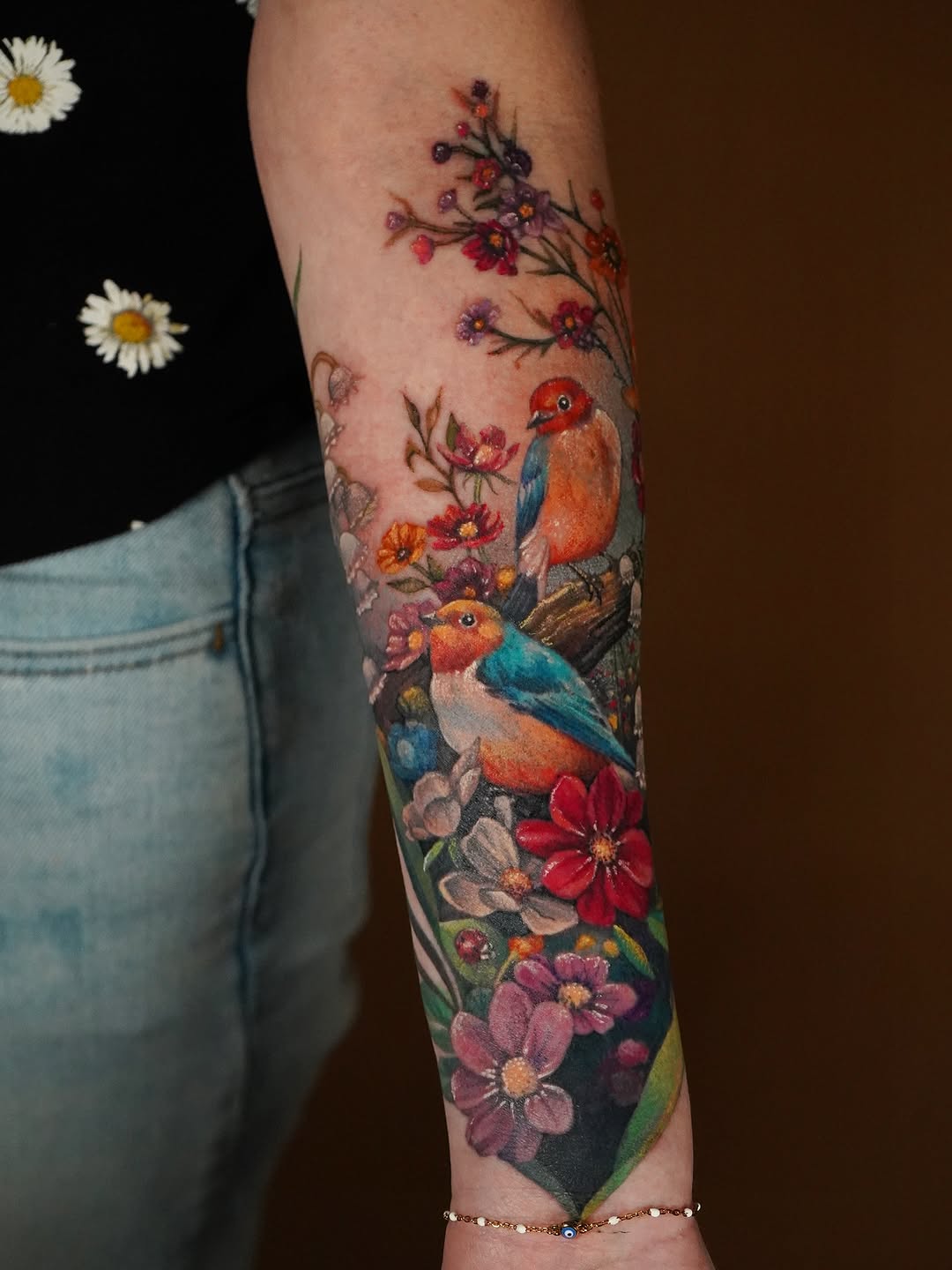 Two red-breasted birds perched among colorful flowers in full bloom on the forearm.