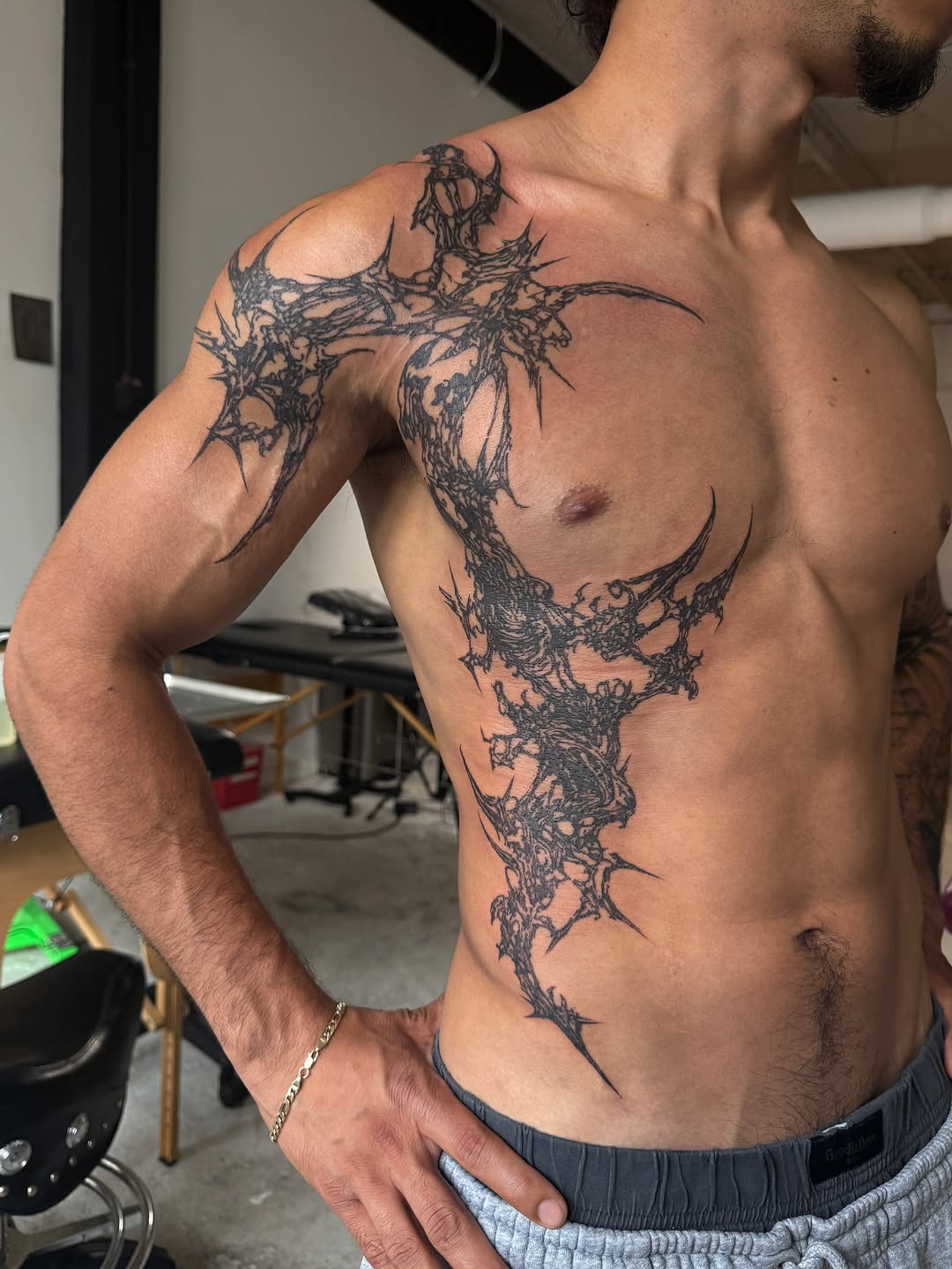 Large-scale dark ornamental tattoo with spiky branching organic forms covering shoulder, chest, and torso area.