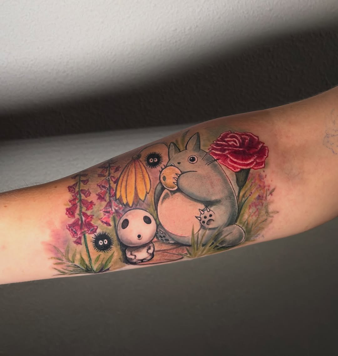 Totoro character holding a red rose surrounded by flowers and soot sprites on forearm.