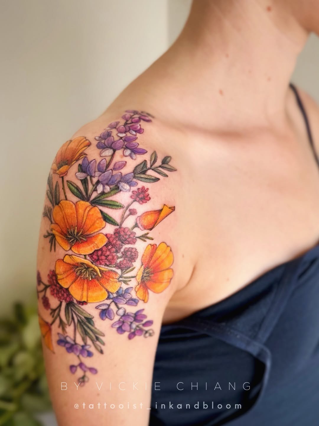 Colorful bouquet of orange poppies, purple wisteria, and pink flowers with green foliage on upper arm and shoulder.