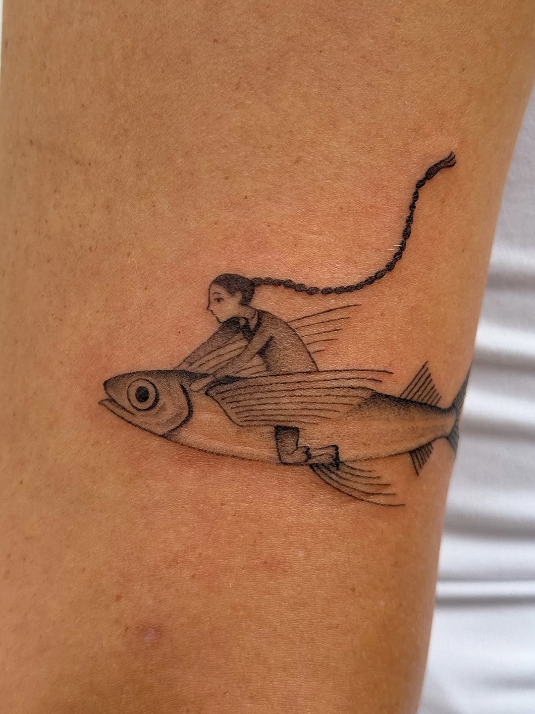 A small figure riding on a fish with a curved line extending upward, rendered in thin black linework on the leg.