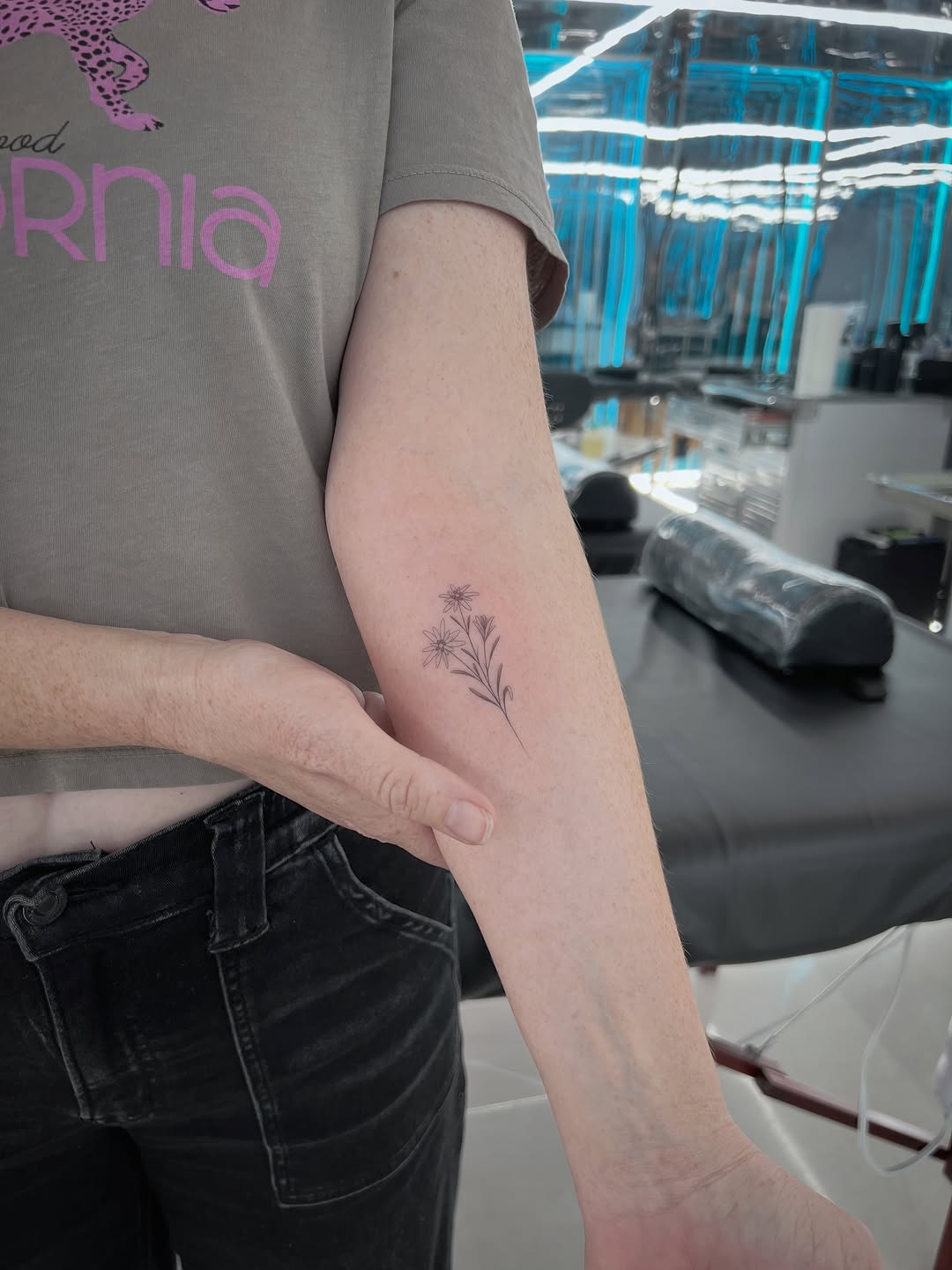 Delicate thin-line floral tattoo with small star and dandelion-like flowers on inner forearm.
