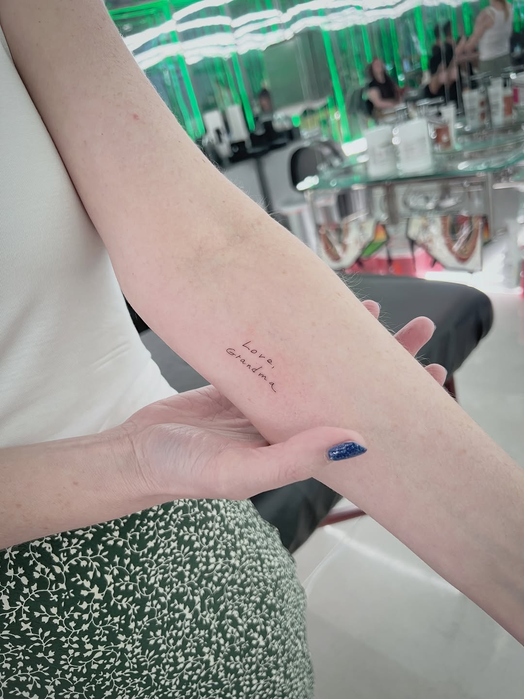 Small delicate fine-line text tattoo reading 'Love Grandma' on inner forearm with minimal linework.
