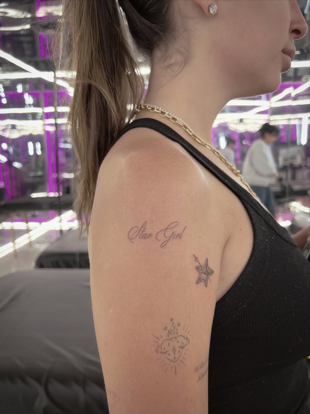 Script text 'Star Girl' with star and ornamental heart designs on upper arm in thin linework.