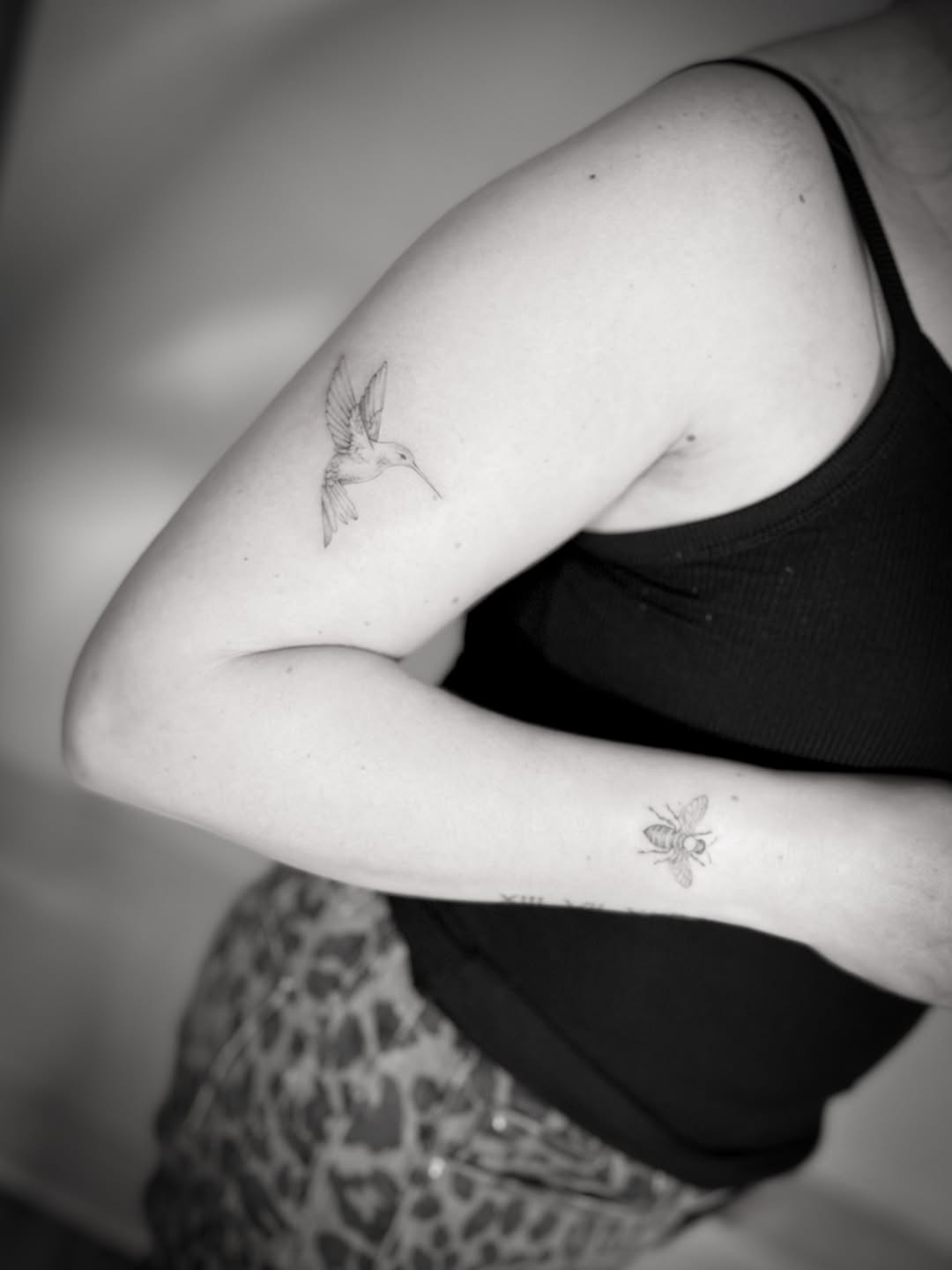 Two delicate fine-line hummingbird tattoos on inner arms in black ink with minimal detail.