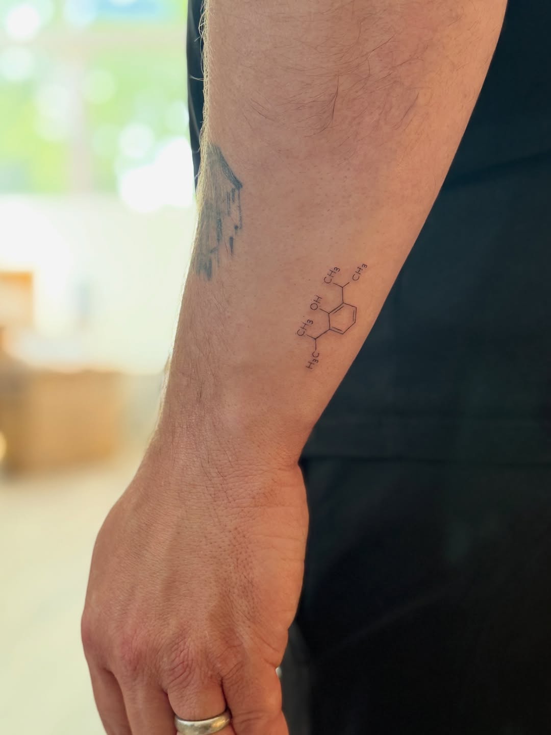 Chemical structure diagram of a molecular compound rendered in thin linework on the inner forearm.