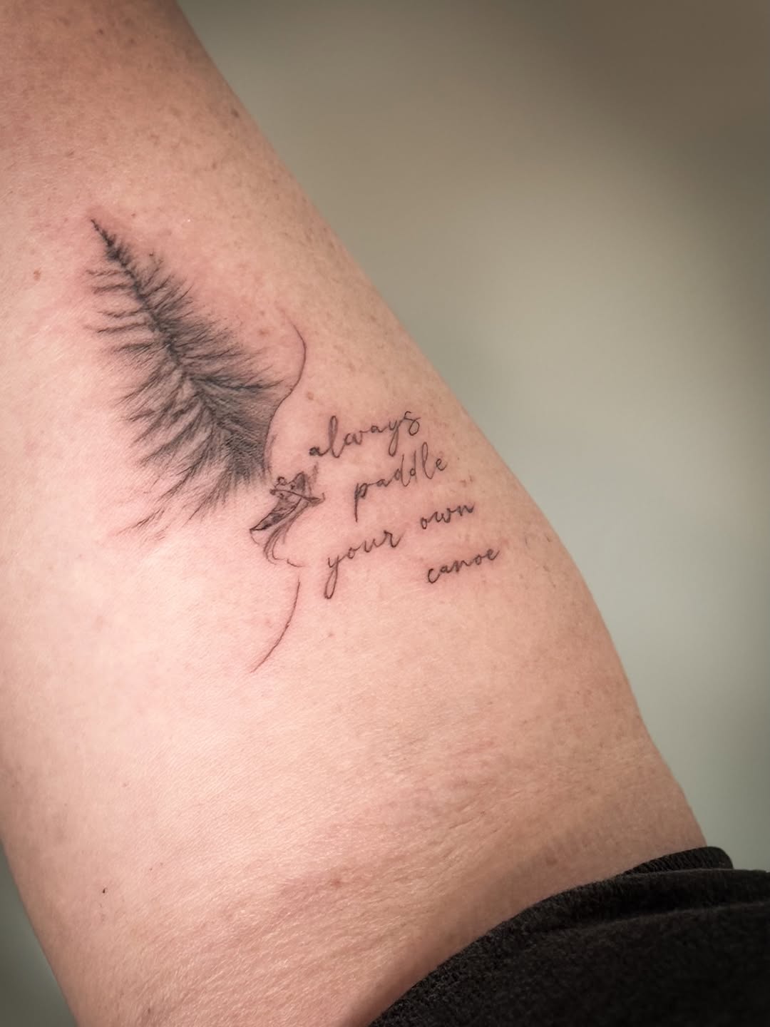 Delicate fine-line wing with script text reading 'always paddle your own canoe' on upper arm.