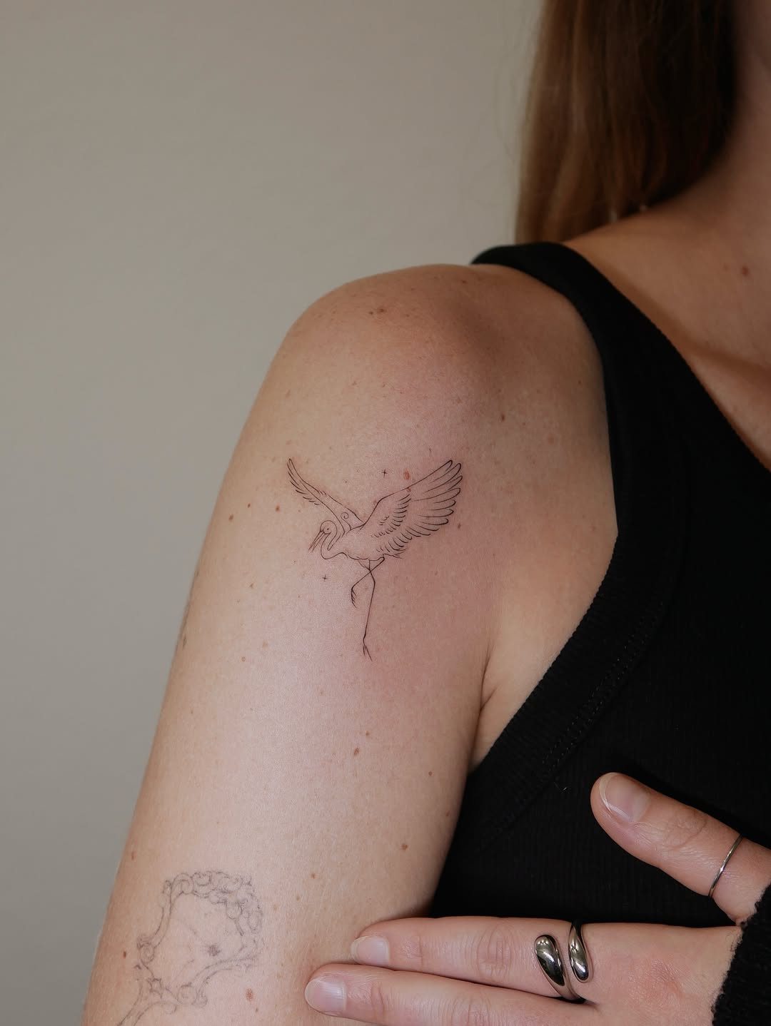 Minimalist line-drawn crane with extended wings and long legs on upper arm.