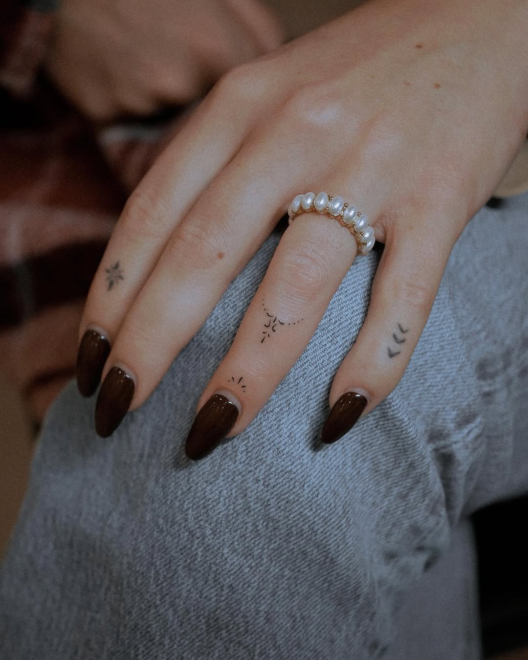 Delicate fine-line constellation and dotwork designs on fingers and hand of person wearing pearl ring.