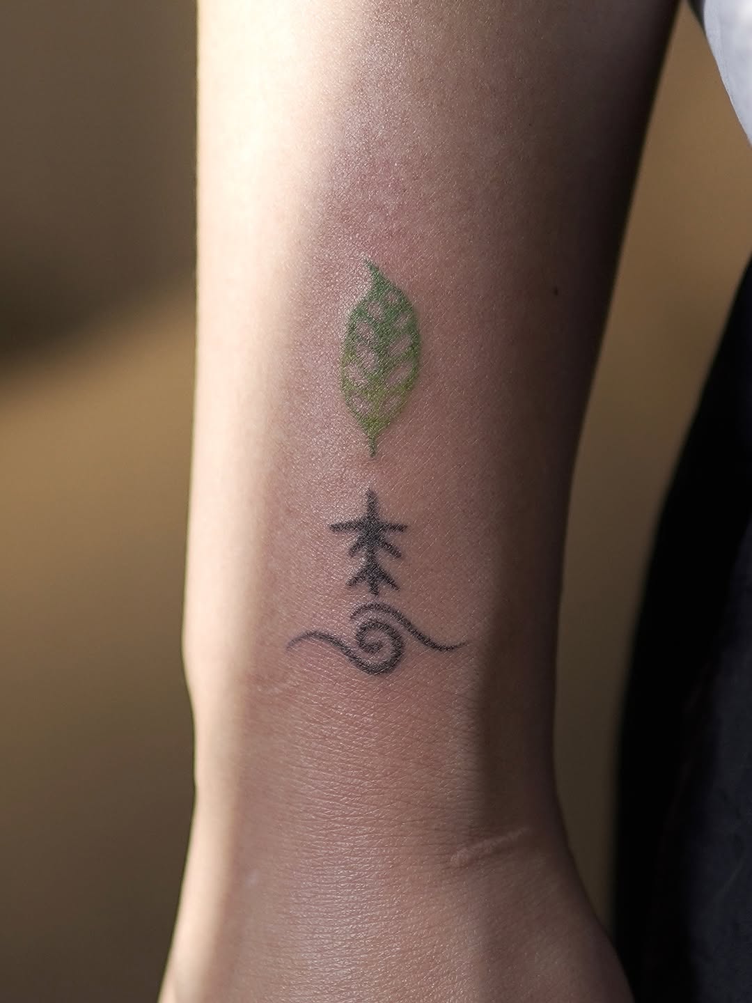 Small fine-line botanical design with a leaf and root system on inner arm, minimalist linework.