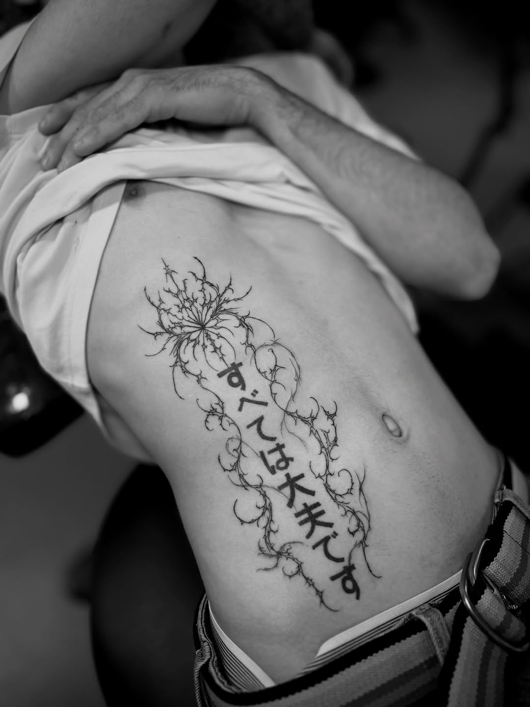 Delicate flowering plant with thin linework and vertical script text running down the side of the torso.