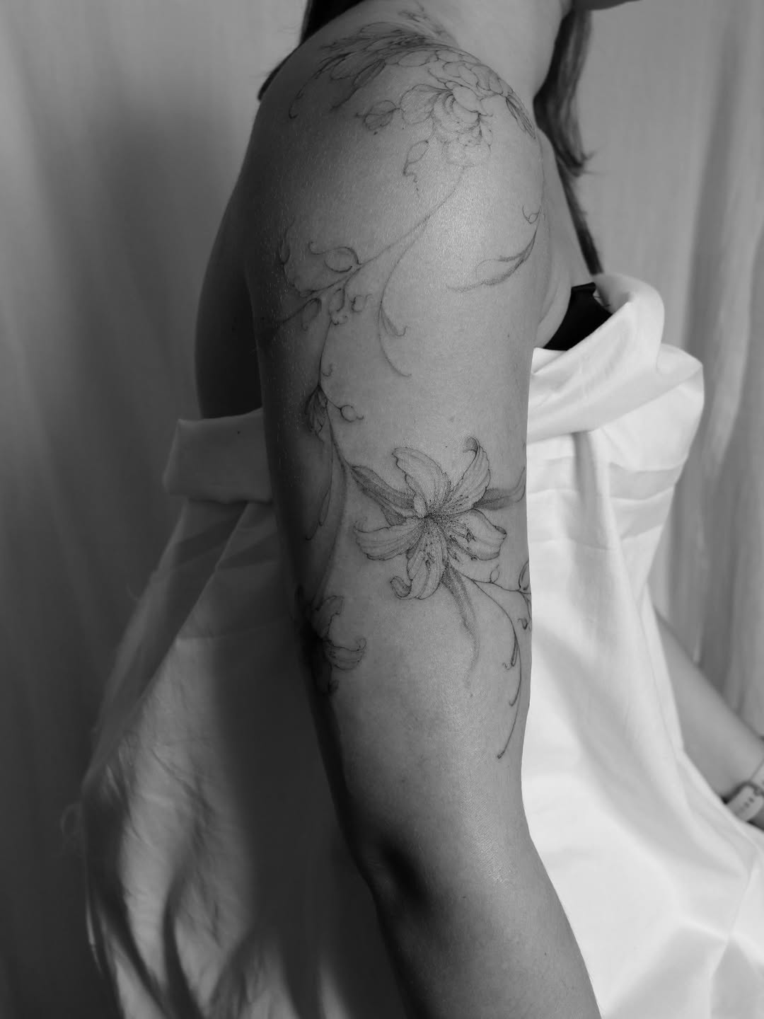 Delicate botanical line work featuring flowering vines and leaves wrapping around the upper arm and shoulder.