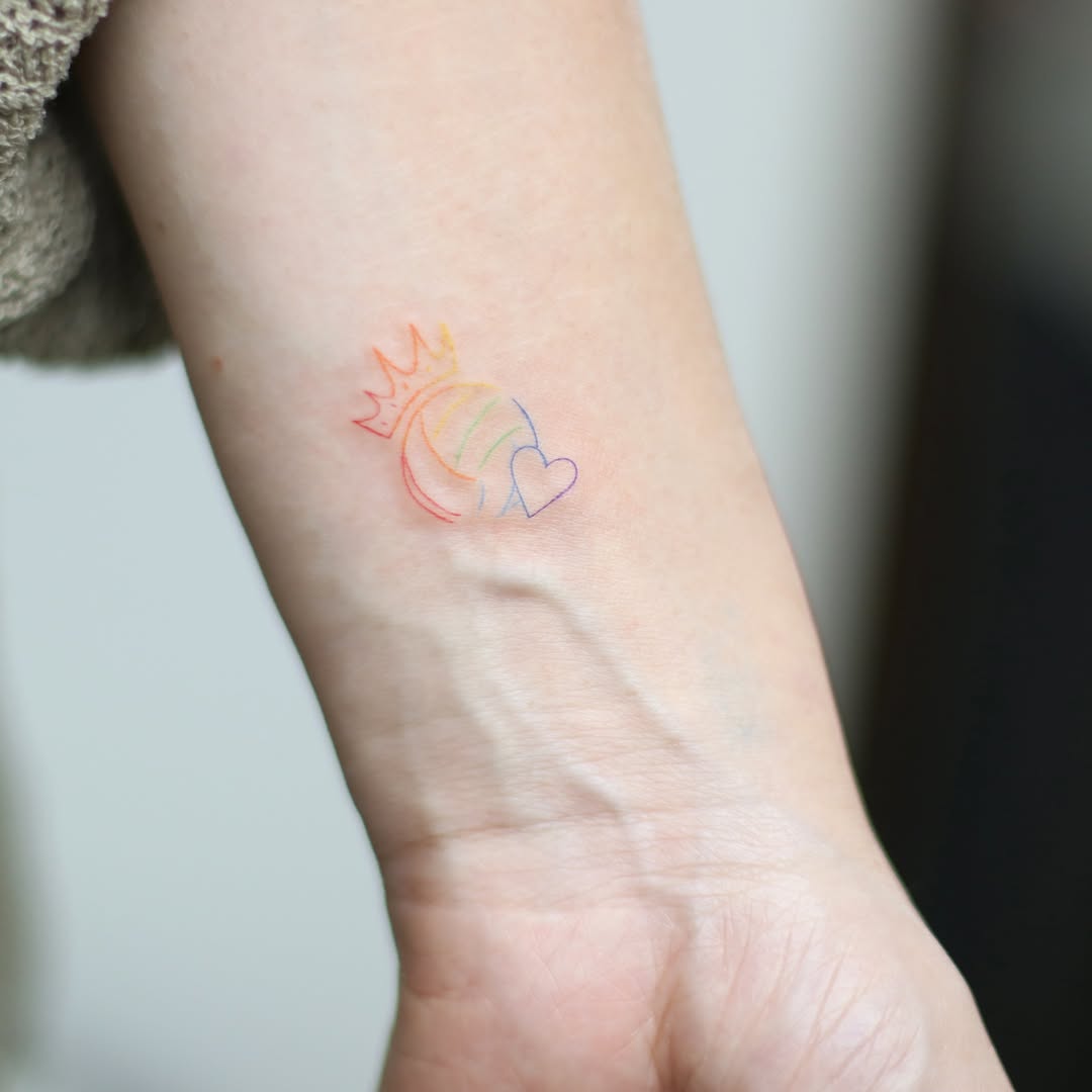 Delicate multi-color fine line tattoo of a crown, heart, and crescent moon on inner forearm.
