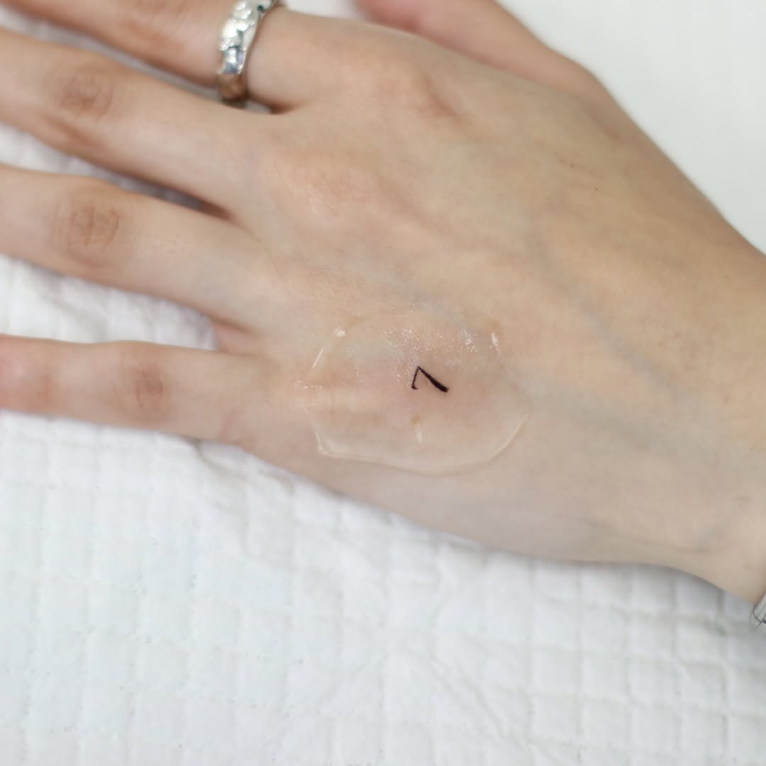 Small minimalist number seven tattoo on the hand with thin linework, placed on the back of the hand near the knuckles.