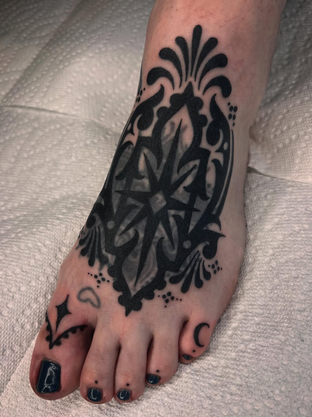 Ornamental geometric mandala-style tattoo with symmetrical linework and dotwork stippling on the foot and ankle.