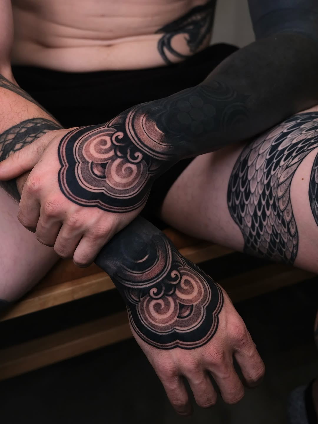 Ornamental geometric hand tattoos featuring symmetrical scrollwork and scale pattern bands on both hands.