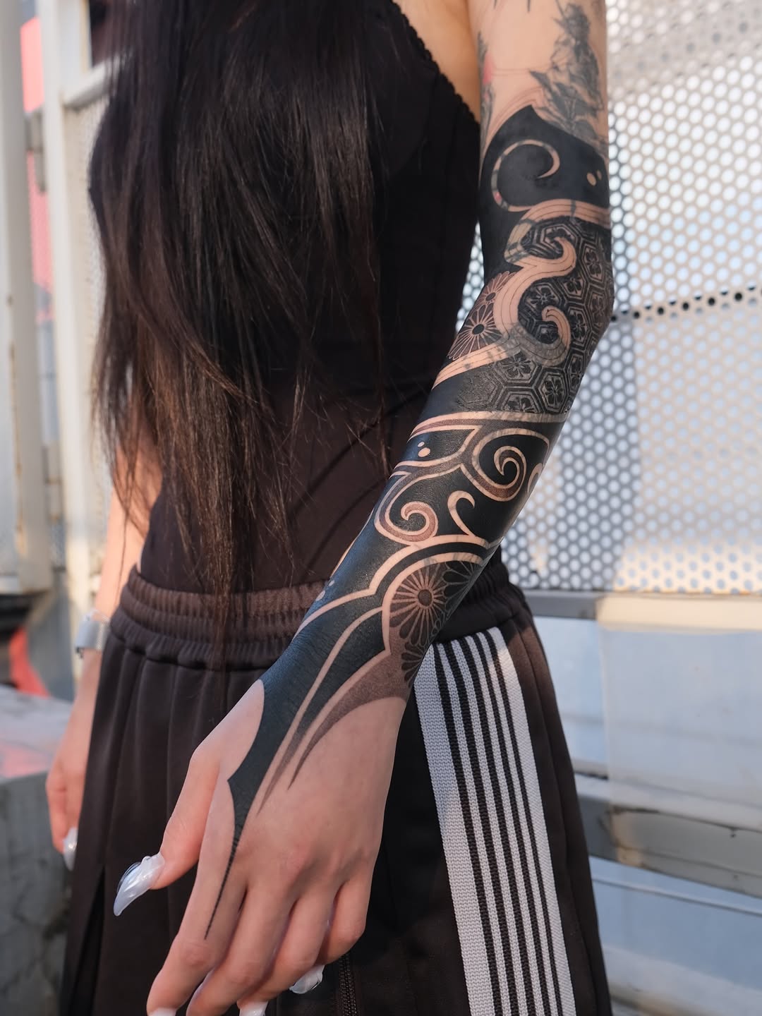 Full-sleeve ornamental mandala and scrollwork tattoo in black and copper tones with symmetrical geometric patterns on the arm.